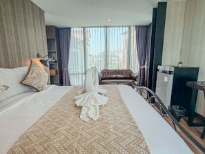 A hotel room with a bed, a sofa, a desk, and a view of the city through large windows. - Chiang Mai Thai House (Chiang Mai)