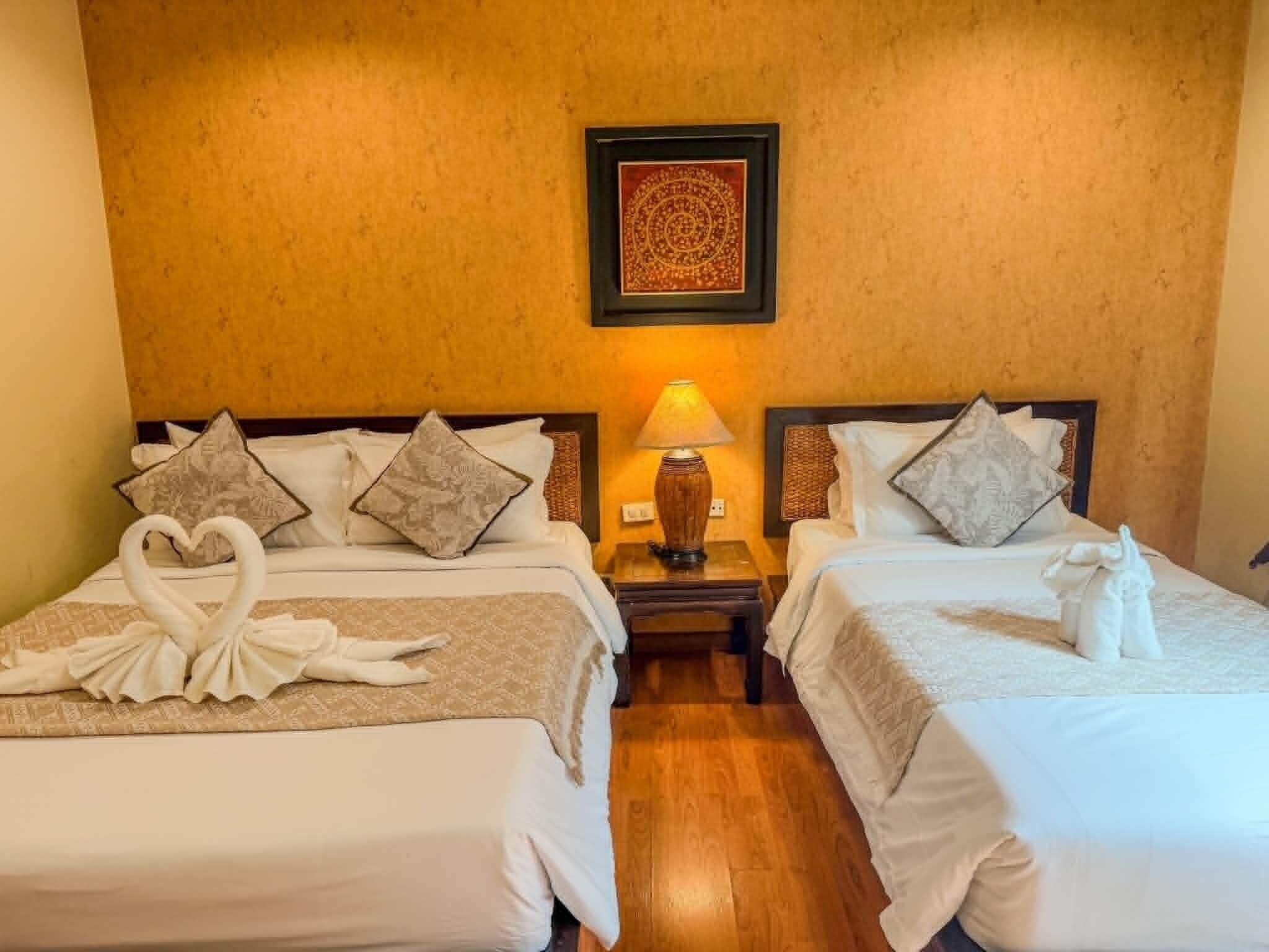 A hotel room with two beds, a nightstand with a lamp, and a framed artwork on the wall.