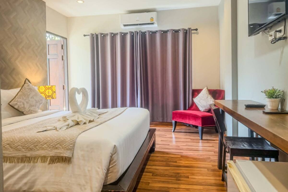 Een hotelkamer met een bed, een rode stoel, een bureau, een televisie en een airconditioning.