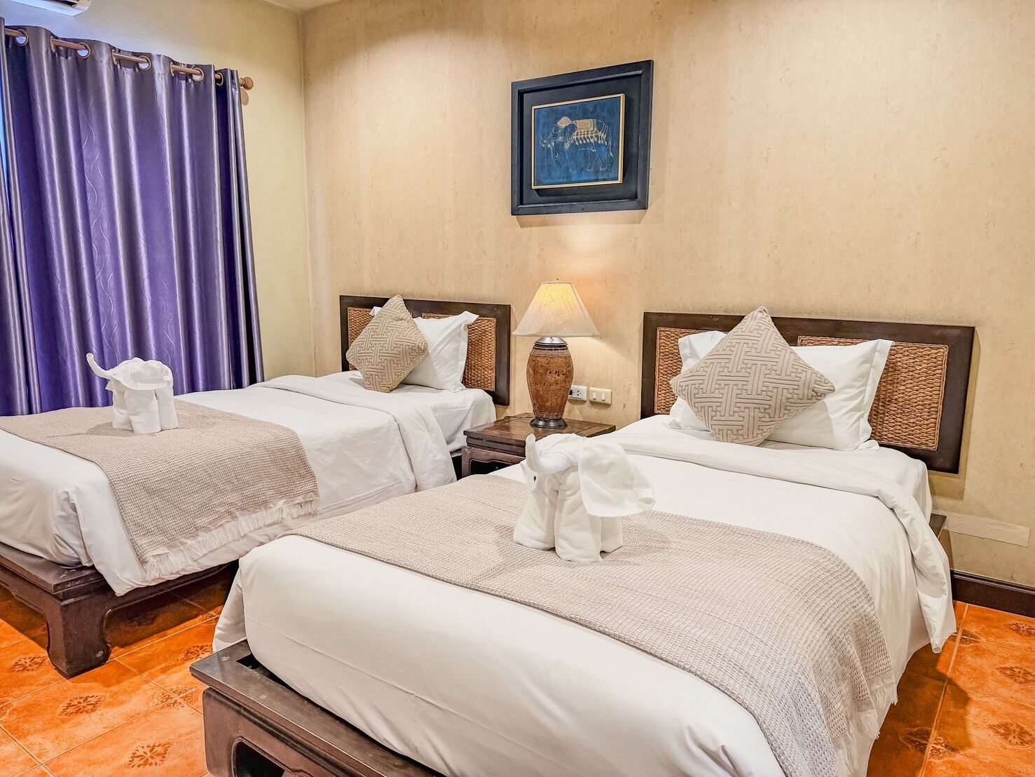 Habitación de hotel con dos camas, una mesita de noche con lámpara, un cuadro enmarcado en la pared y una cortina.