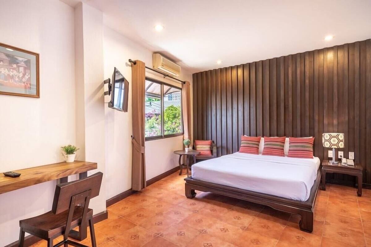 Een hotelkamer met een bed, een bureau met stoel, een kleine tafel en een aan de muur bevestigde televisie.