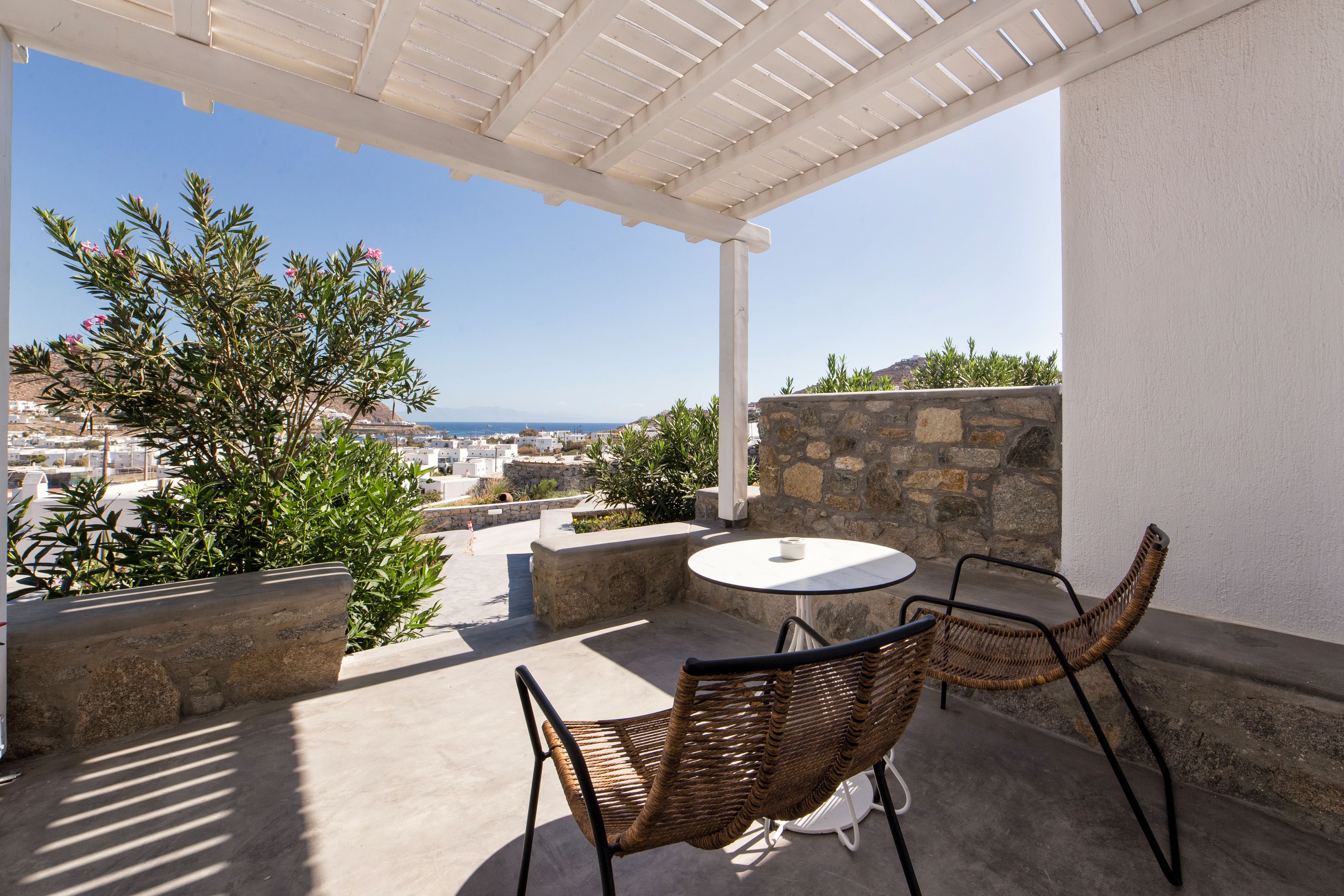 An outdoor patio with a round table and wicker chairs, overlooking a coastal cityscape.