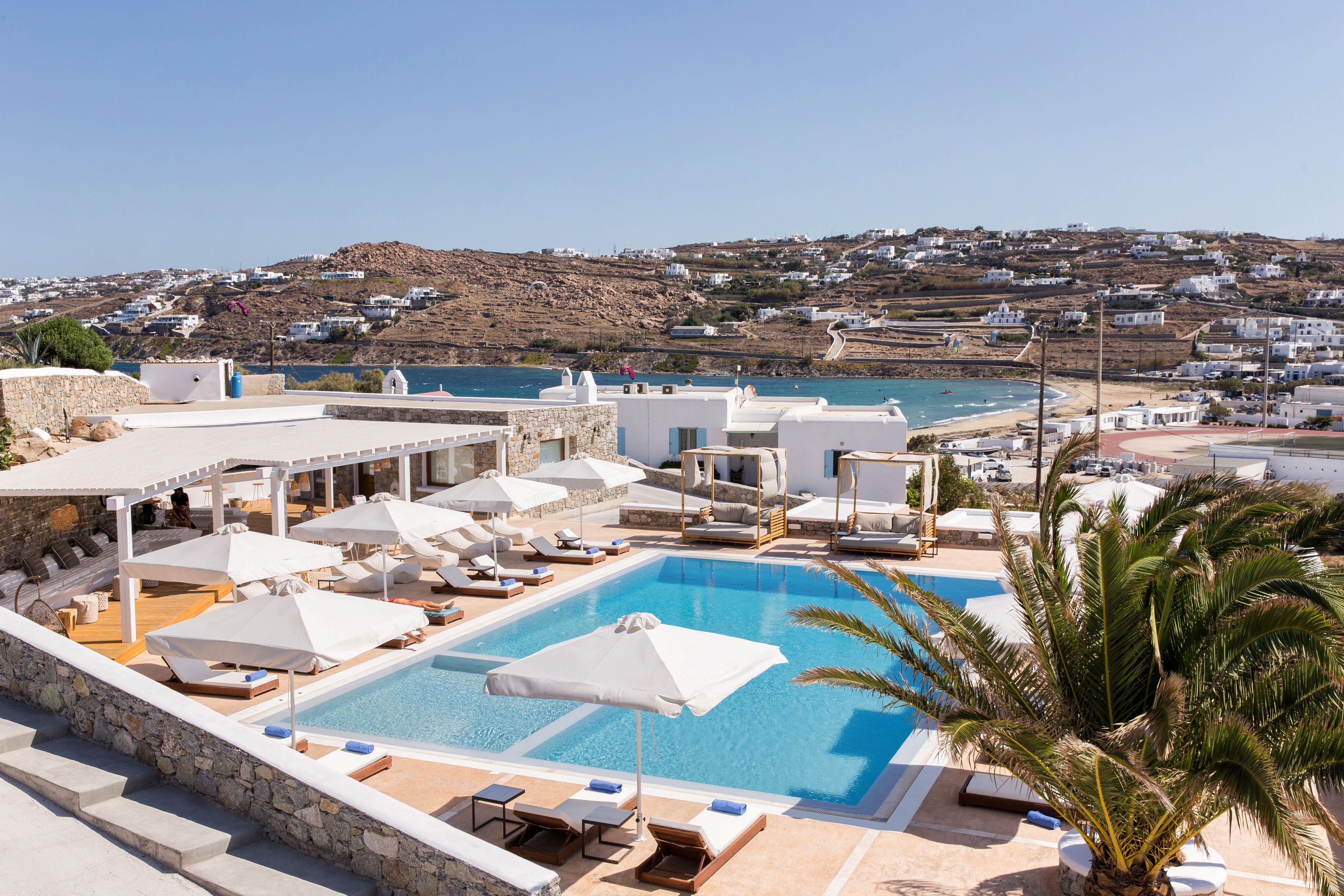 A pool area with lounge chairs and umbrellas, overlooking a coastal town with white buildings.