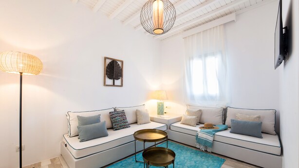 A modern living room with a sectional sofa, a standing floor lamp, a small round table, and a blue patterned rug. - Osom Resort (Mykonos)
