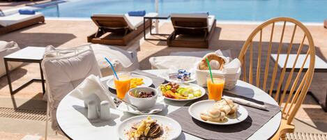 A table with breakfast items and a view of a pool with lounge chairs.