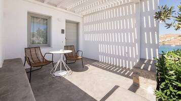Un patio con una pérgola blanca, dos sillas de mimbre, una mesita redonda y vistas a una piscina y jardines.