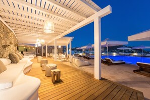 Une terrasse en bois avec des chaises longues et un espace piscine, agrémenté d’un mur en pierre et de mobilier blanc.