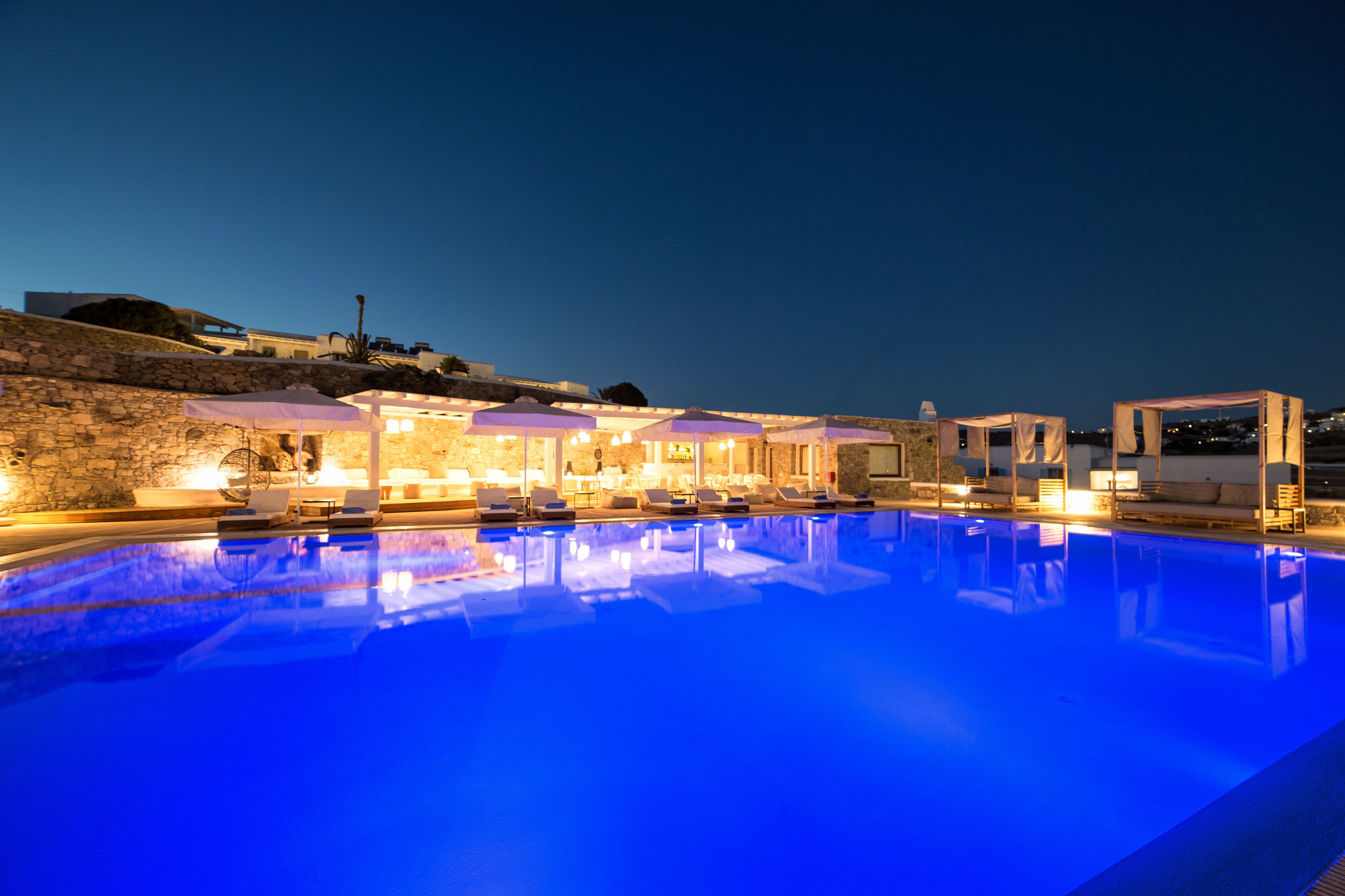 A swimming pool with lounge chairs and umbrellas, surrounded by stone walls and a building with outdoor seating.