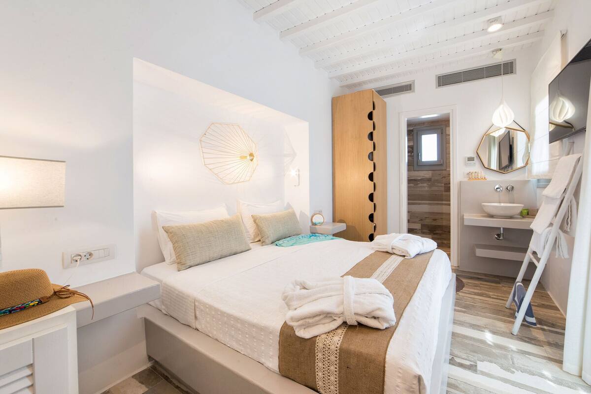 A hotel room with a bed, bedside table, wall-mounted light, and a bathroom with a sink and mirror.