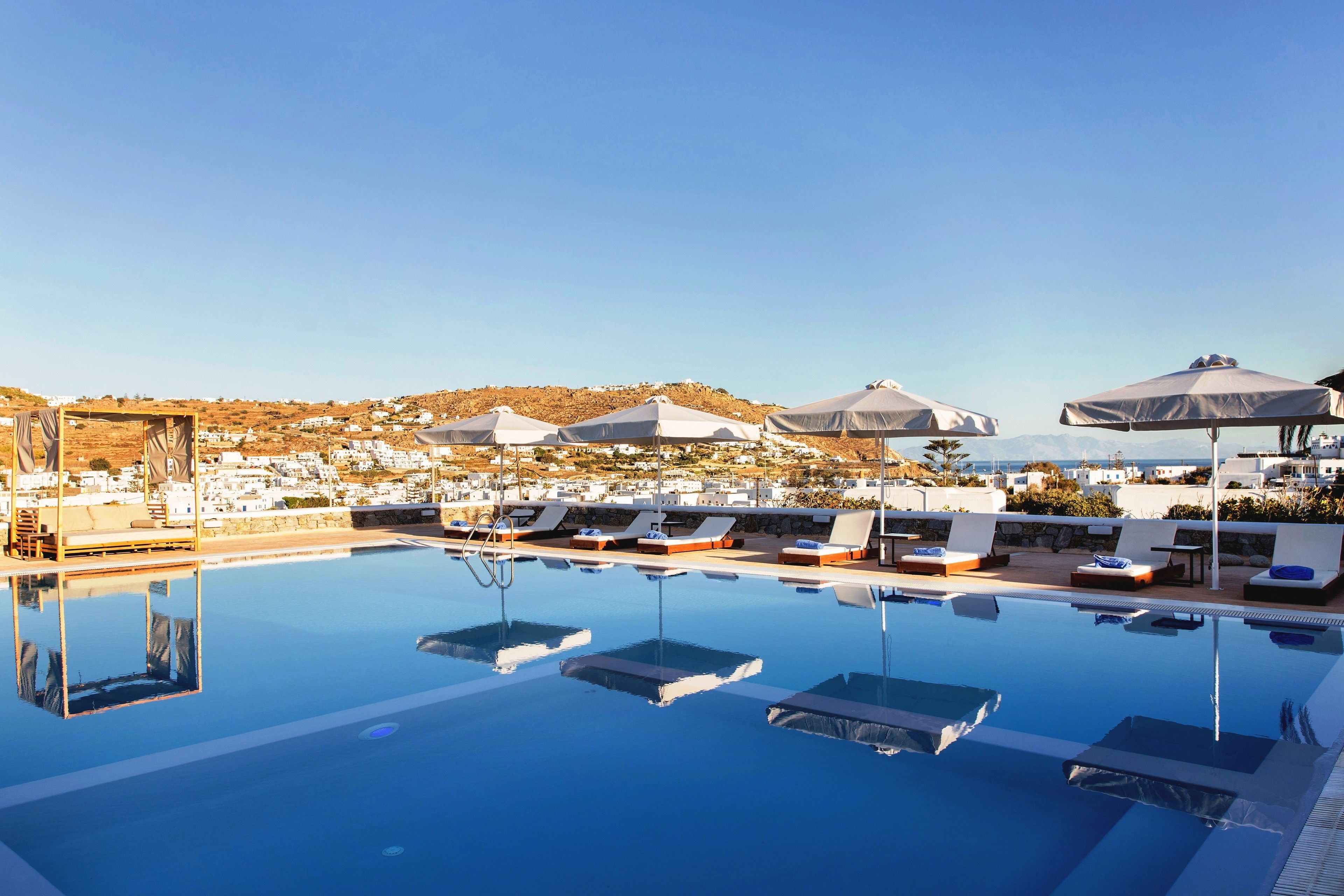 A clear blue pool with lounge chairs and umbrellas, overlooking a coastal village.