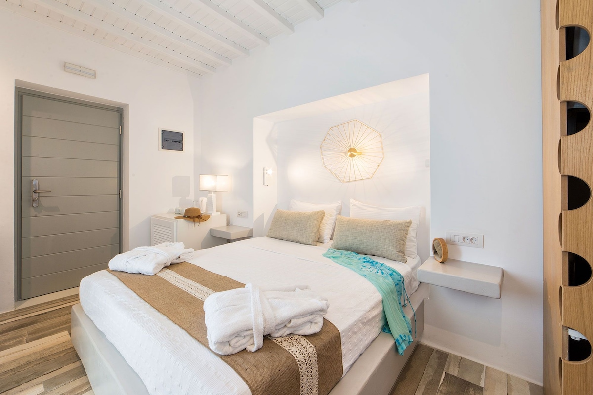 Quarto de hotel moderno com uma cama grande, mesas de cabeceira, luminária fixada na parede e uma porta.