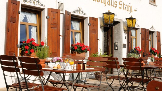 Een terras met houten tafels en stoelen, potplanten en een bordje met de tekst 'Gasthaus Stuhl'.
