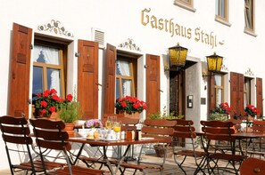 An outdoor cafe with wooden tables and chairs, potted plants, and a sign reading "Gasthaus Stuhl". - Gasthaus Weingut Stahl (Oberwesel)