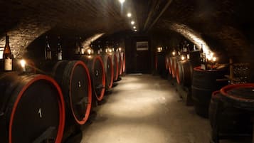 A wine cellar with rows of barrels and bottles, illuminated by overhead lights.