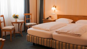 Een hotelkamer met twee bedden, een klein rond tafeltje met een bloevas, een stoel, een nachtkastje met een lamp en een spiegel aan de muur.