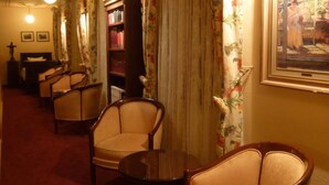 Een hotelkamer met een rood tapijt, twee fauteuils, een kleine tafel, een boekenkast en een schilderij aan de muur.
