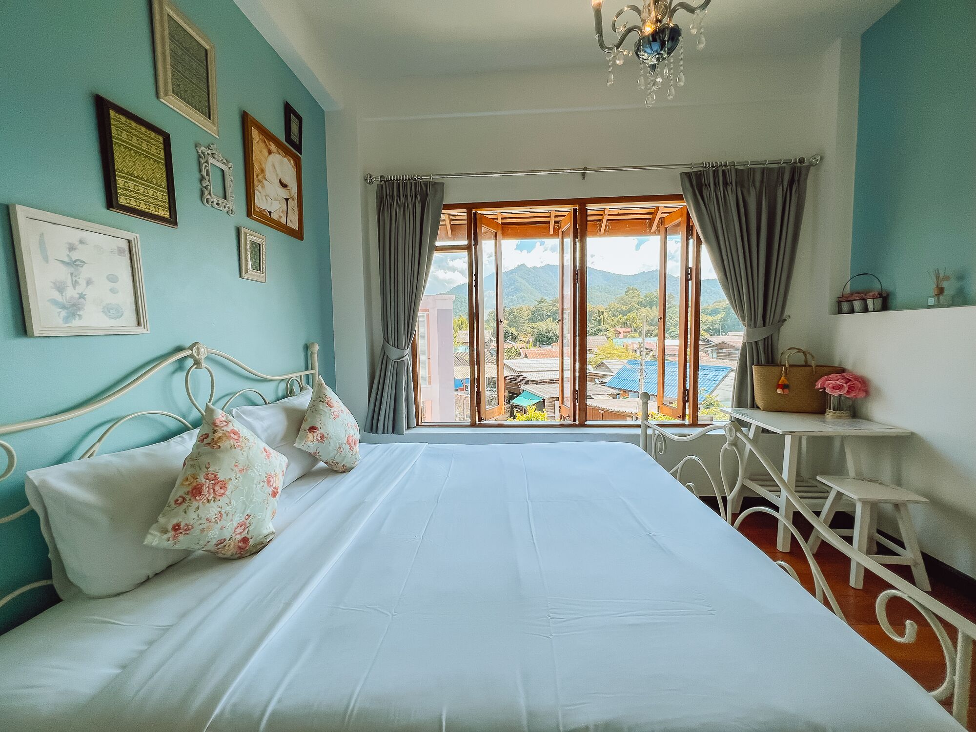 Ein Schlafzimmer mit Bett, einem Fenster mit Vorhängen, einer Kristallleuchtre und Blick auf Gebäude und Berge.