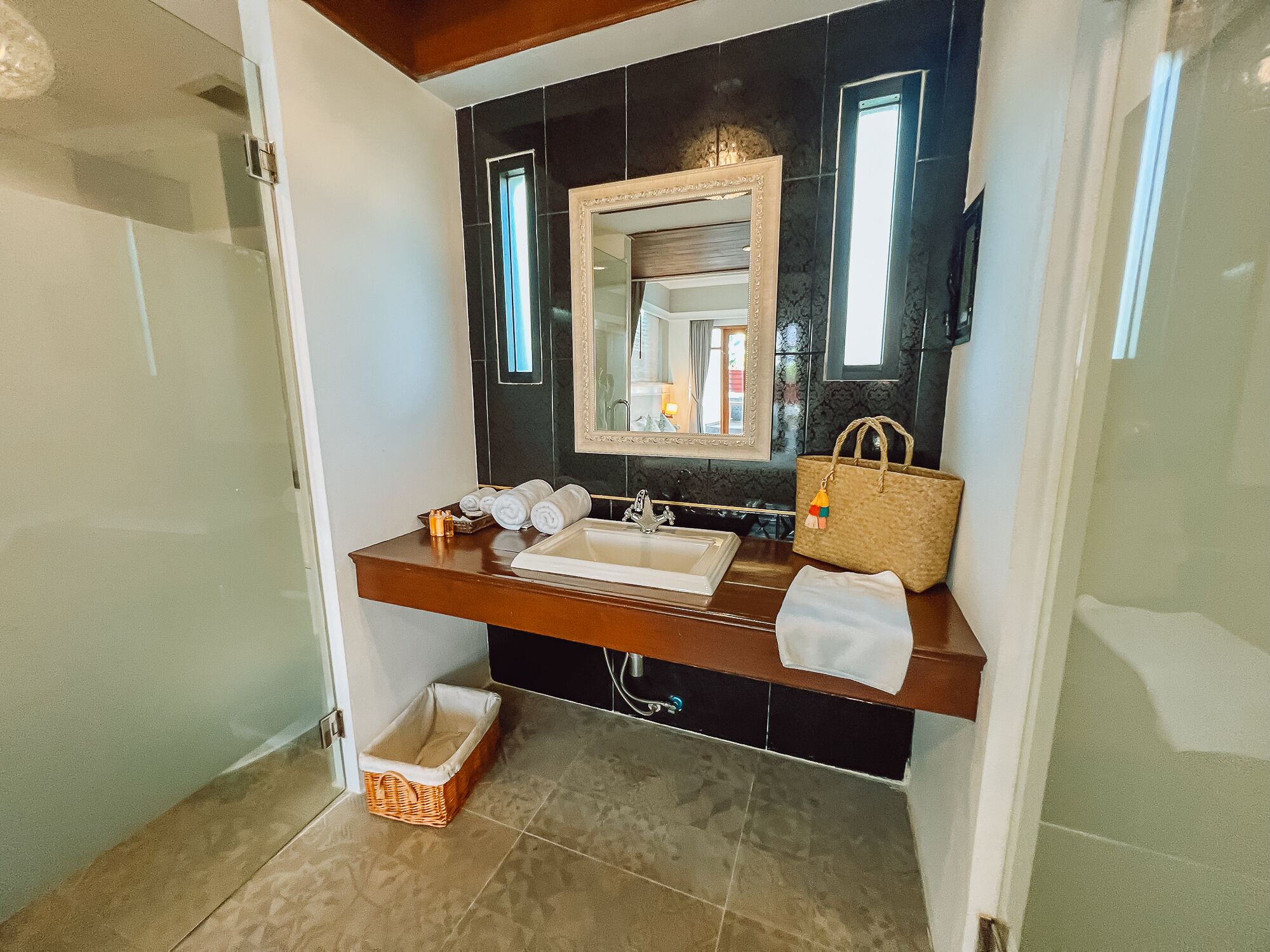 A bathroom with a large mirror, a sink, and a towel rack. There is a wicker basket under the sink and a handbag on the counter.