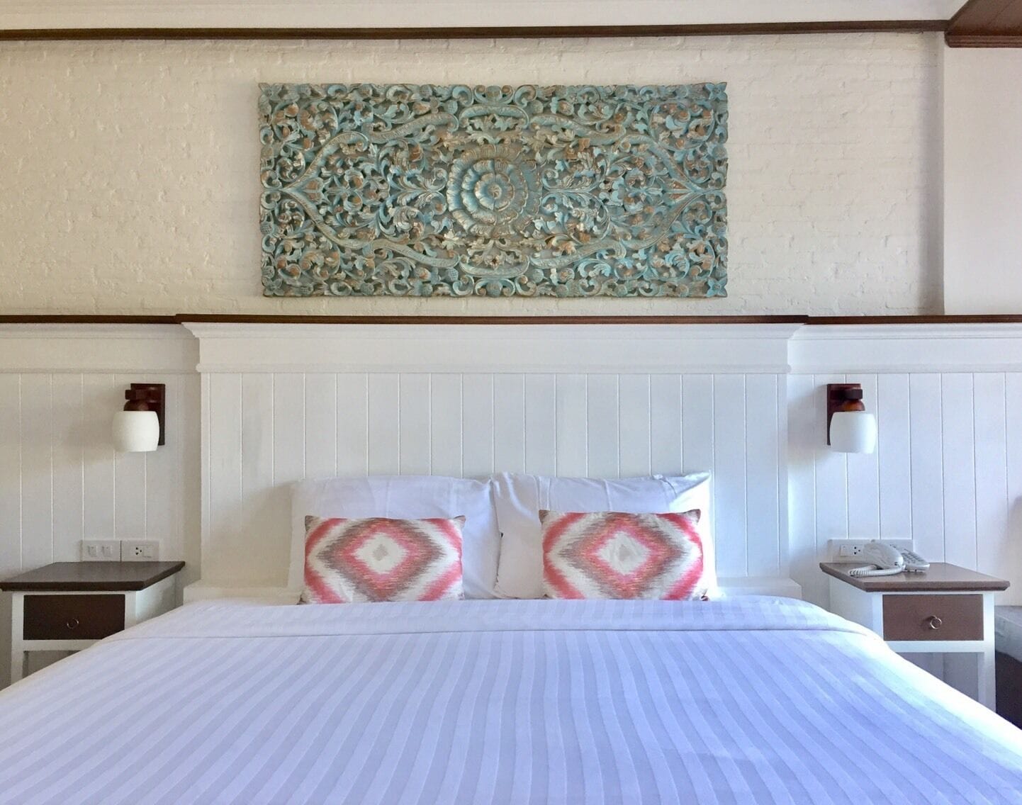 A hotel room with a bed, two nightstands, a wall-mounted artwork, and a white headboard.