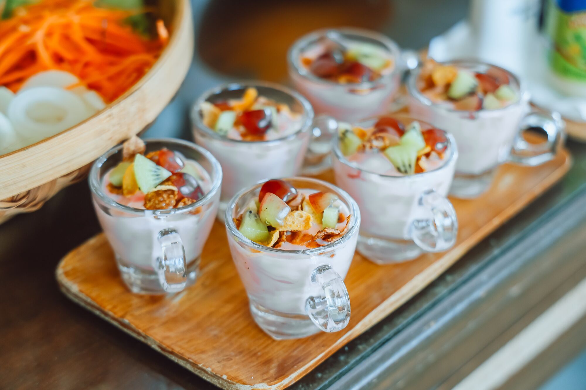 Un vassoio con bicchieri trasparenti contenenti una bevanda a strati e frutta fresca, e un cesto di frutta a fette.