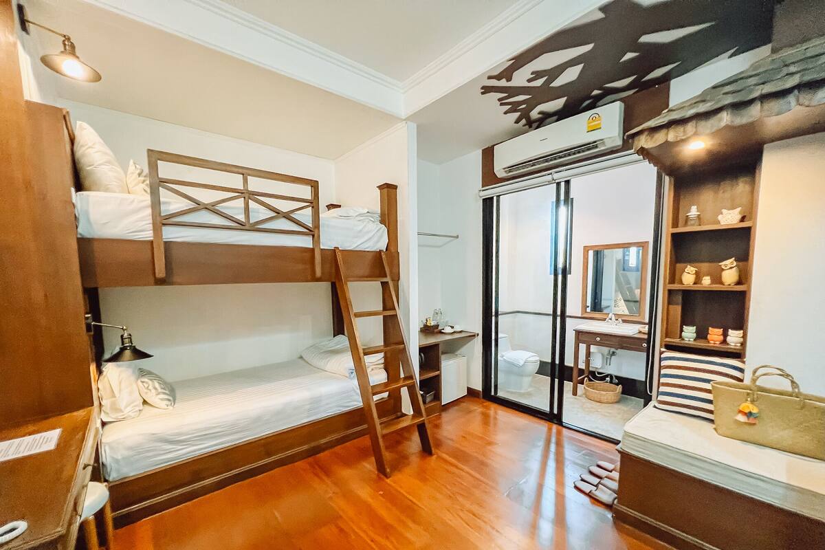 Ein gemütlicher Raum mit Etagenbett, einer Holzleiter, einem kleinen Schreibtisch, einem Spiegel, einem Regal mit Dekoration und einer Schiebetür zum Badezimmer.
