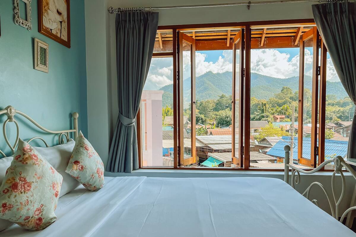 Ein Zimmer mit Bett, einem Vorhangfenster und Blick auf eine Berglandschaft.