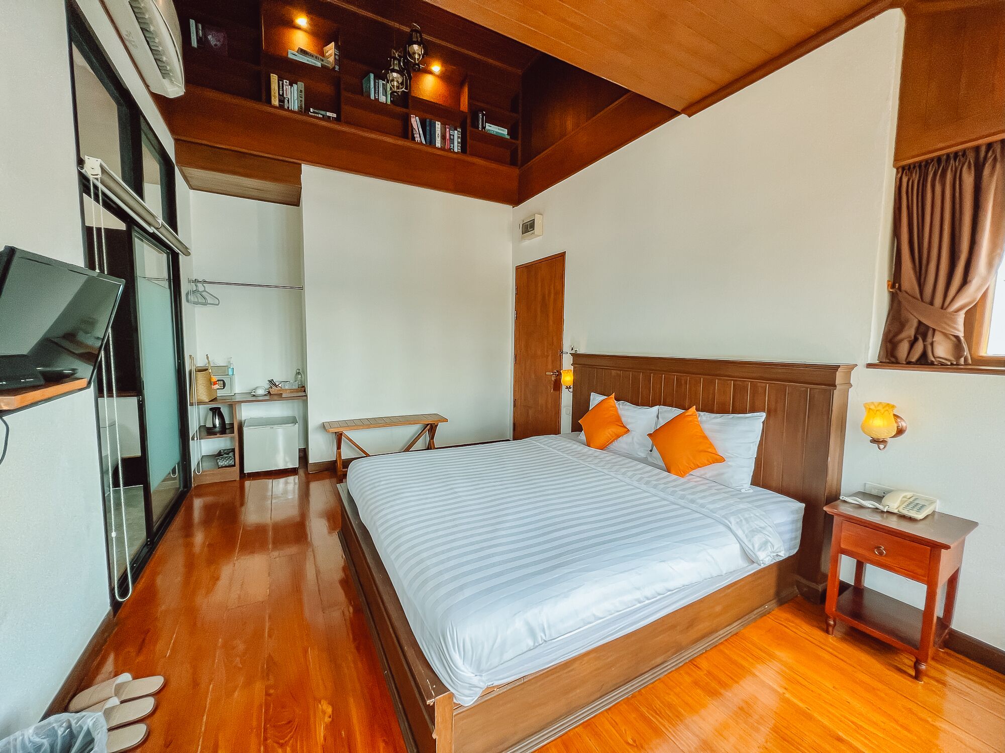 A hotel room with a wooden bed, a desk, a chair, a small table, and a bookshelf.