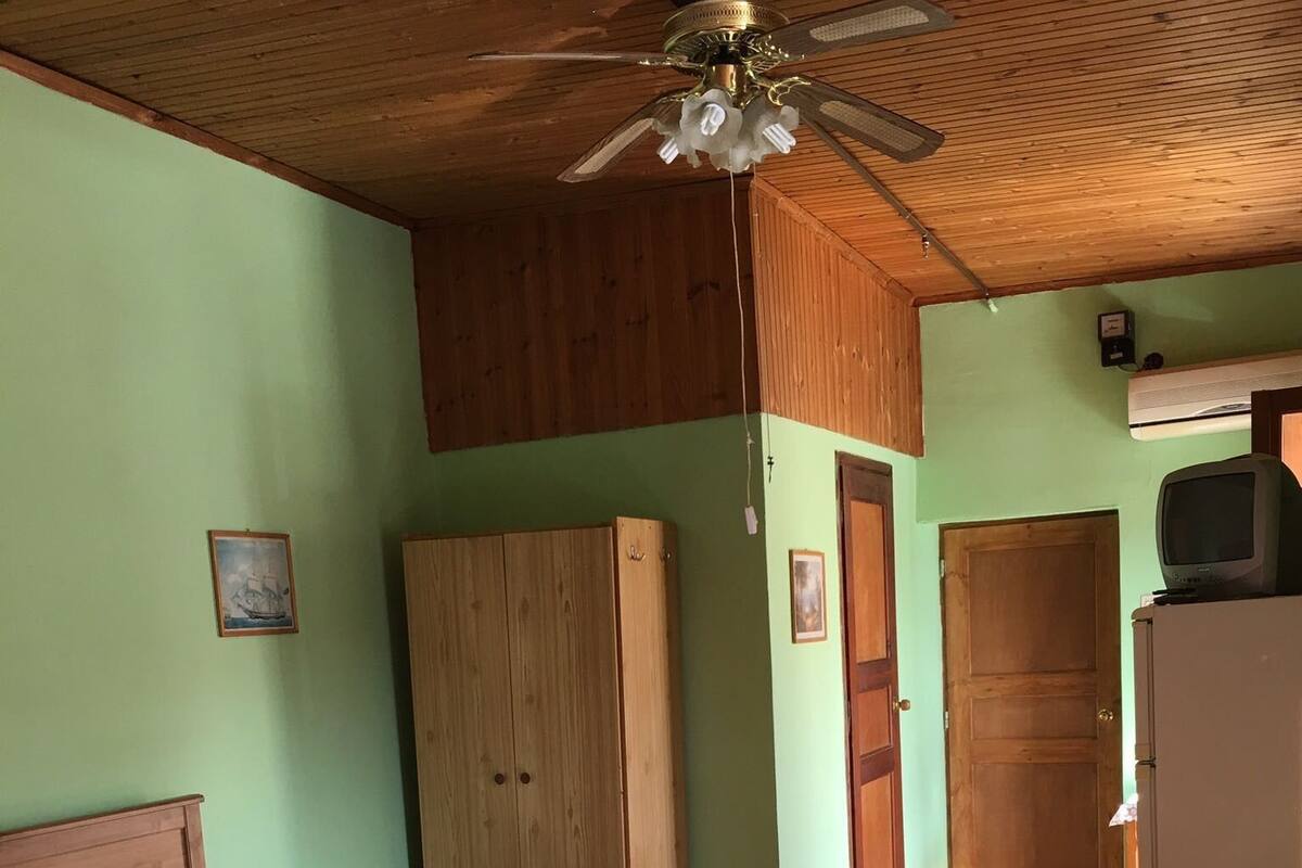 A room with a wooden bed, a wooden wardrobe, a small table with a vase, and a ceiling fan.