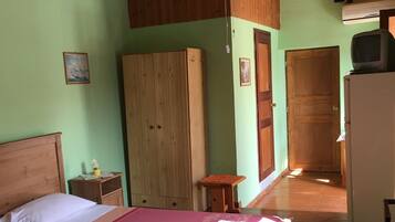 A room with a wooden bed, a wooden wardrobe, a small table with a vase, and a ceiling fan.