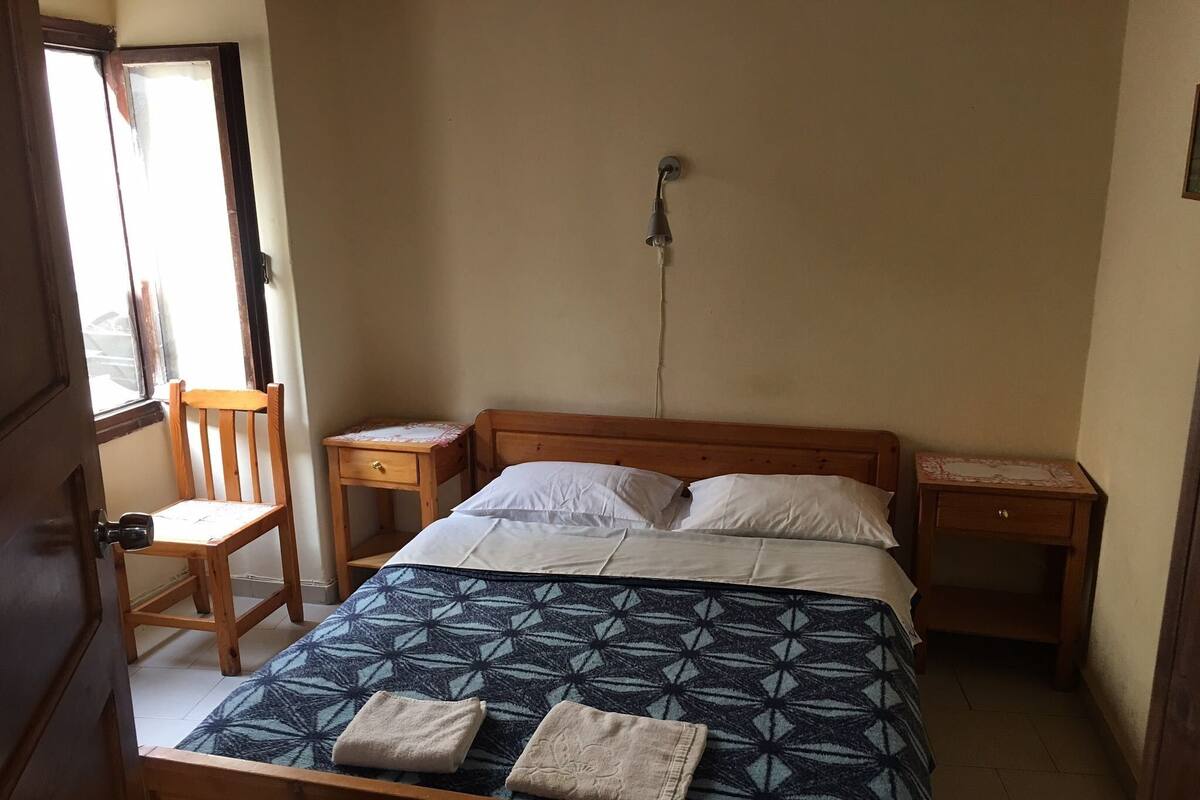 A bedroom with a wooden bed, two bedside tables, a chair, and a window.