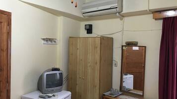 A compact room with a wooden wardrobe, a small white refrigerator, a television on top, a mirror, and a red curtain.