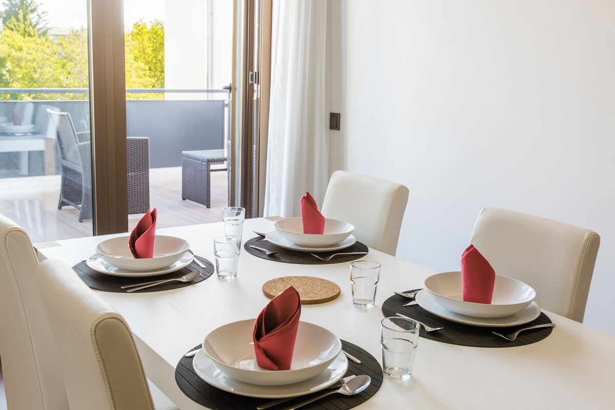 A dining table set for four with white plates, red napkins, and clear glasses.