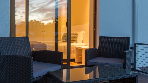 A balcony with wicker chairs and a glass table, overlooking a bedroom with a bed and a nightstand. - Steyler Fatima Hotel Congress (Ourem)