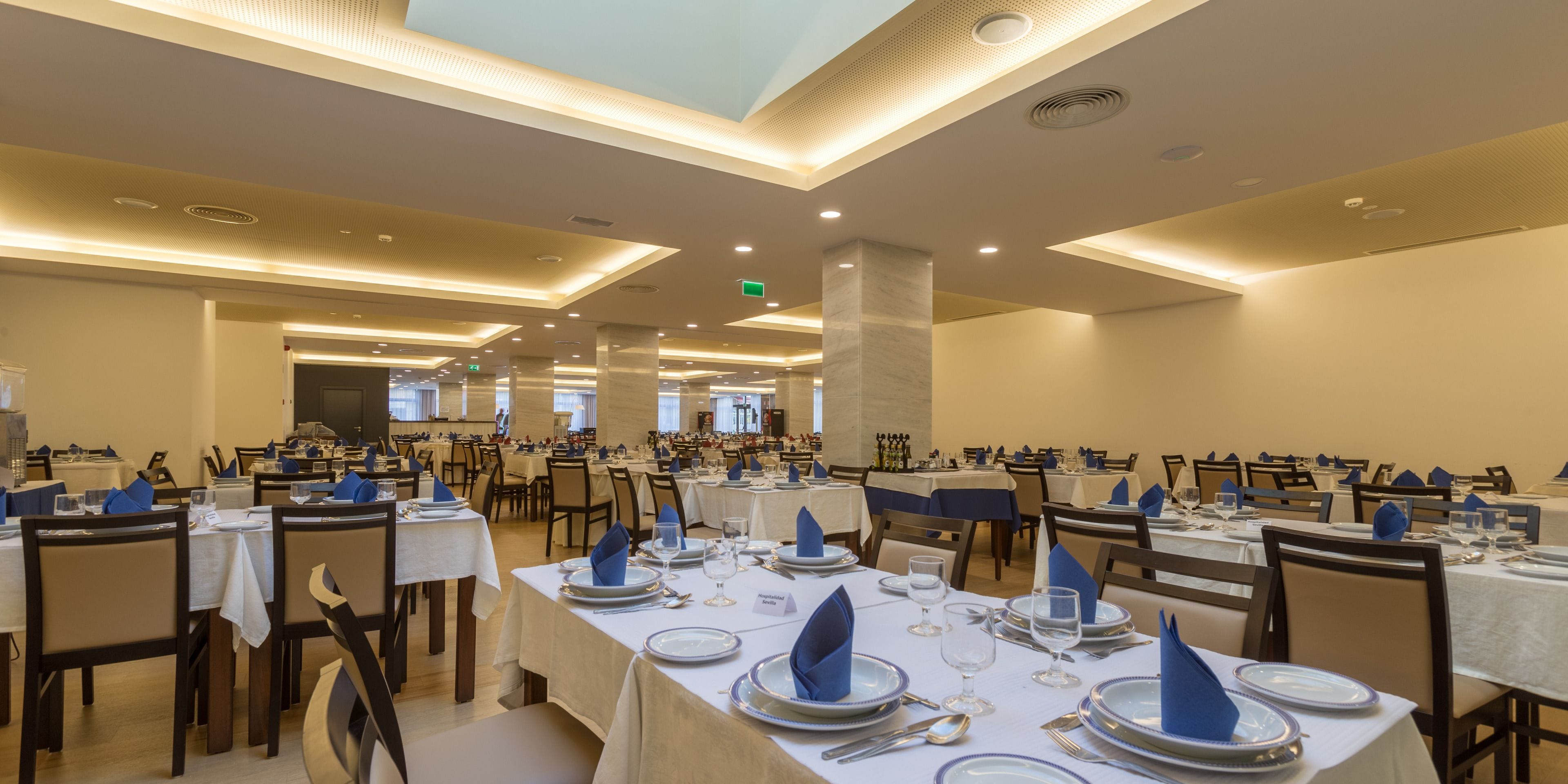 A spacious dining area with multiple tables set for service, featuring a consistent tablecloth and chair design.