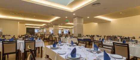 A spacious dining area with multiple tables set for service, featuring a consistent tablecloth and chair design.