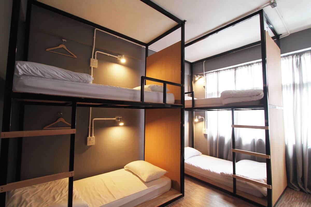 A bunk bed room with a wooden frame, a hanging light fixture, and a window with curtains.