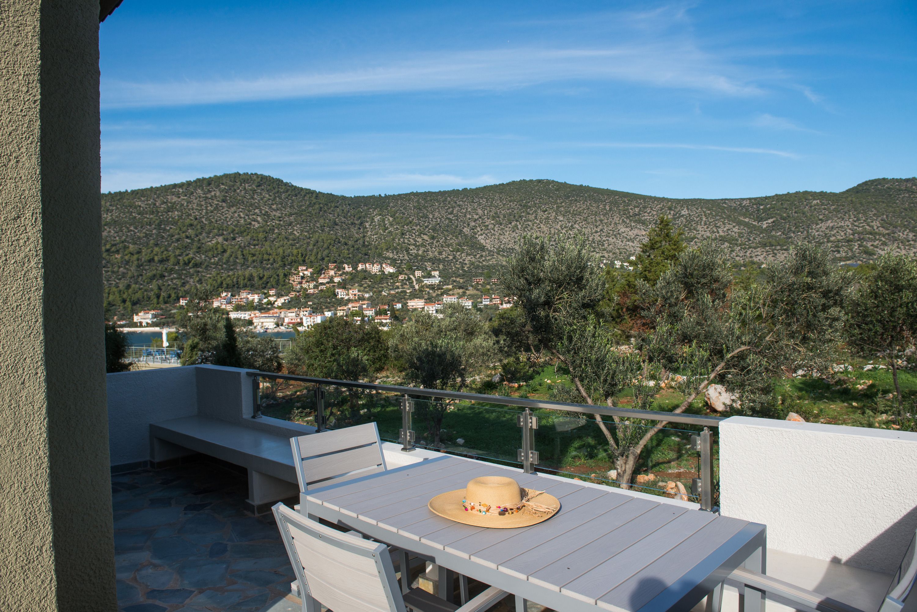 A balcony with a table and chairs, a hat on the table, and a view of a hillside town.