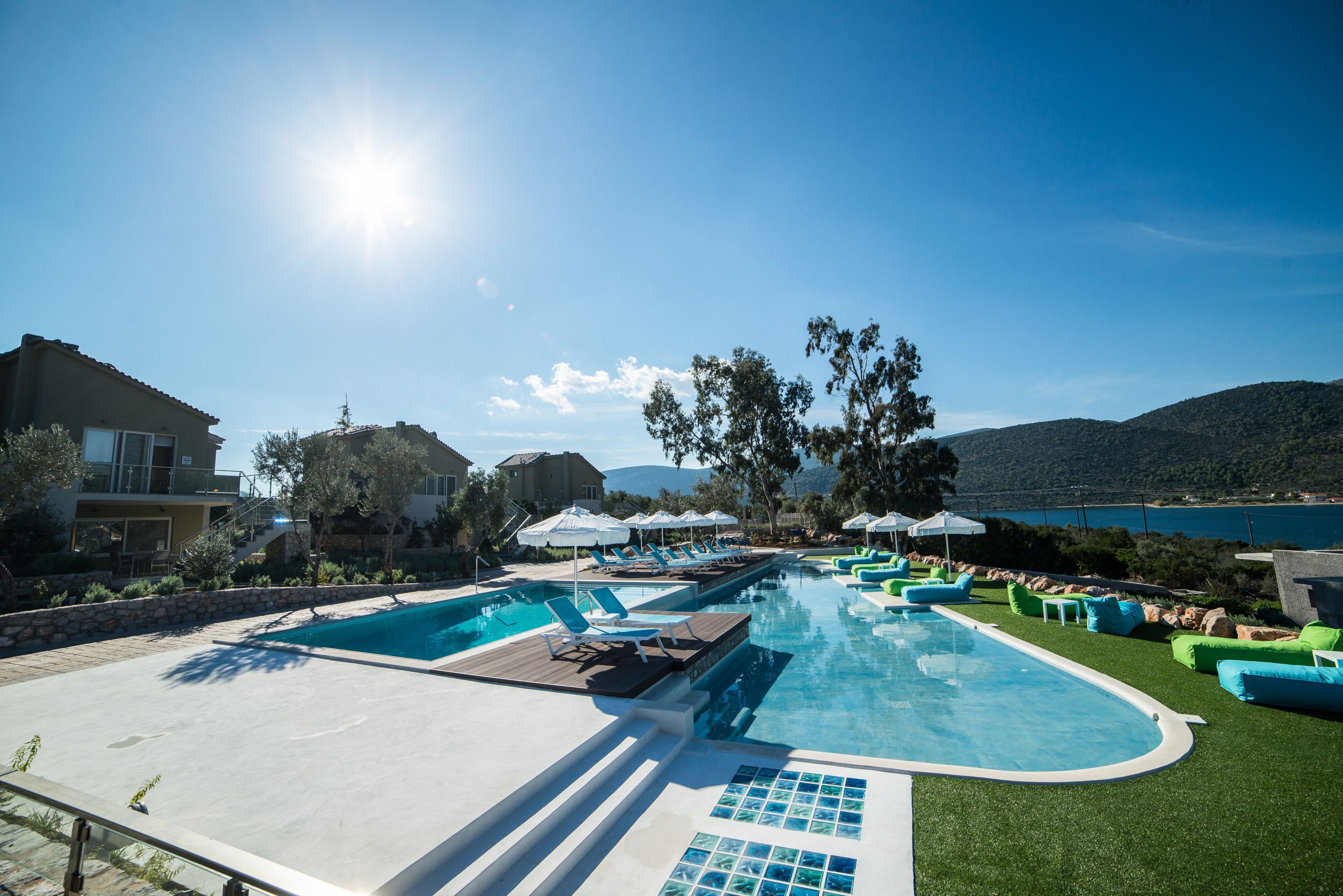 A swimming pool with lounge chairs and umbrellas, surrounded by greenery and a view of the sea.