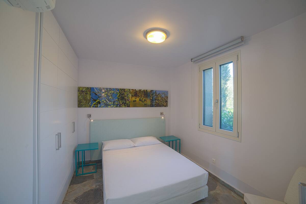 A bedroom with a bed, a window, a painting, and a ceiling light.