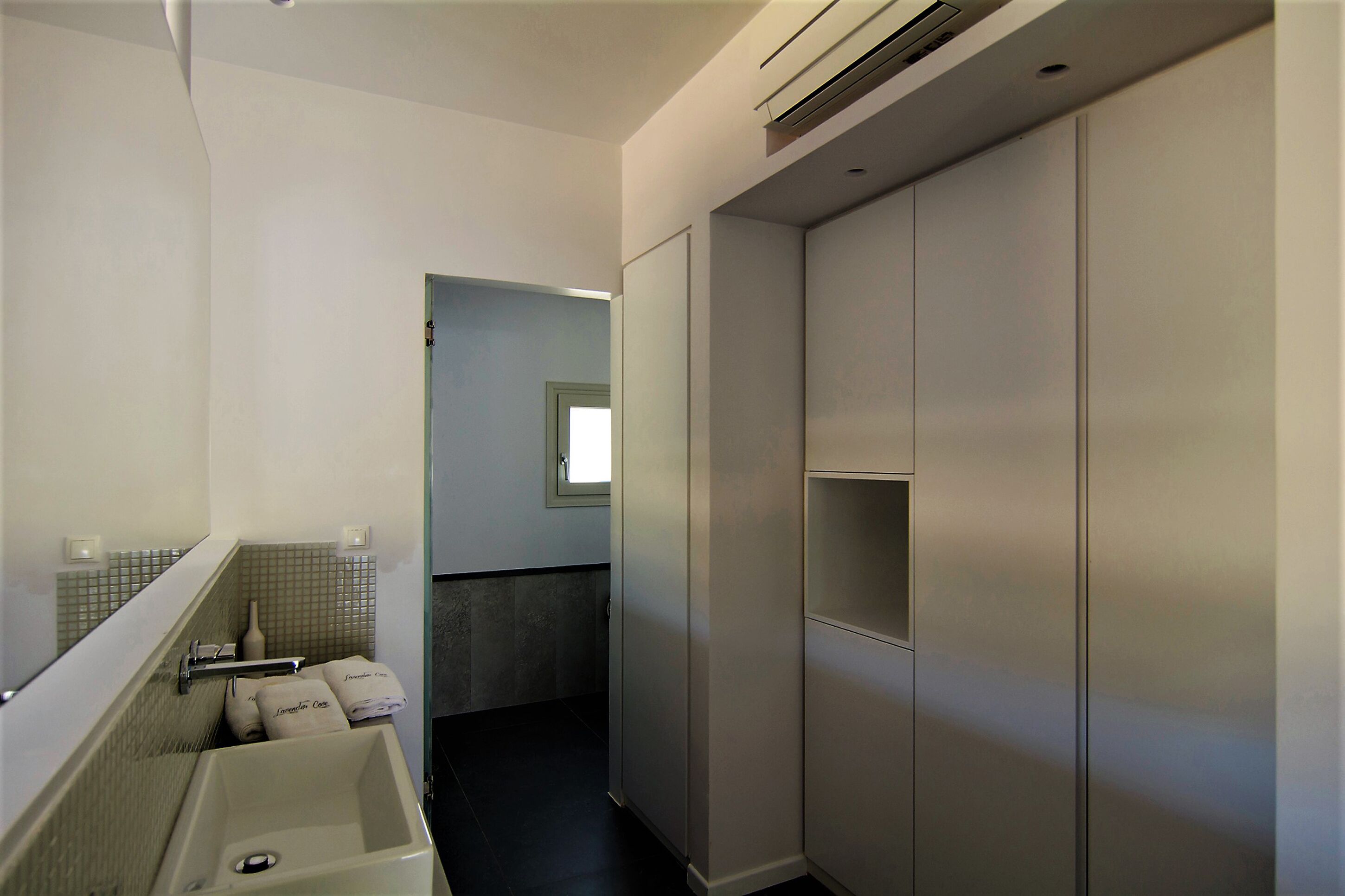 A modern bathroom with a sink, mirror, towel rack, and a walk-in closet.