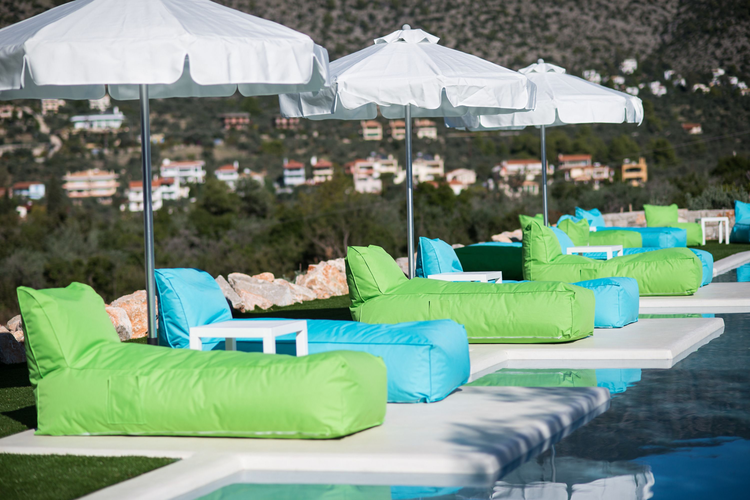 A poolside area with lounge chairs and umbrellas, a clear view of the surrounding landscape, and a pool reflecting the environment.