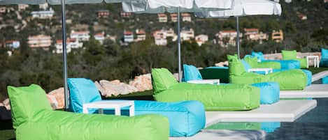 A poolside area with lounge chairs and umbrellas, a clear view of the surrounding landscape, and a pool reflecting the environment.