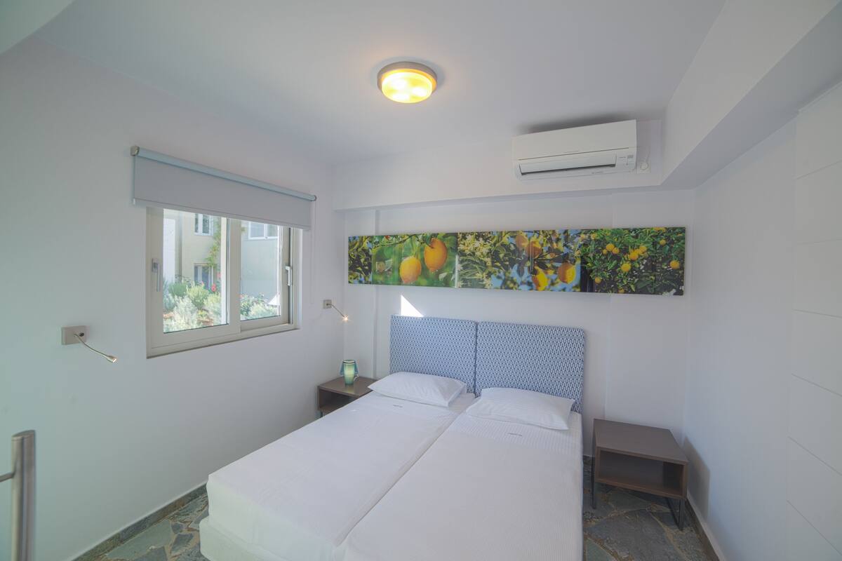 A bedroom with a bed, a nightstand, a window, and an air conditioning unit.
