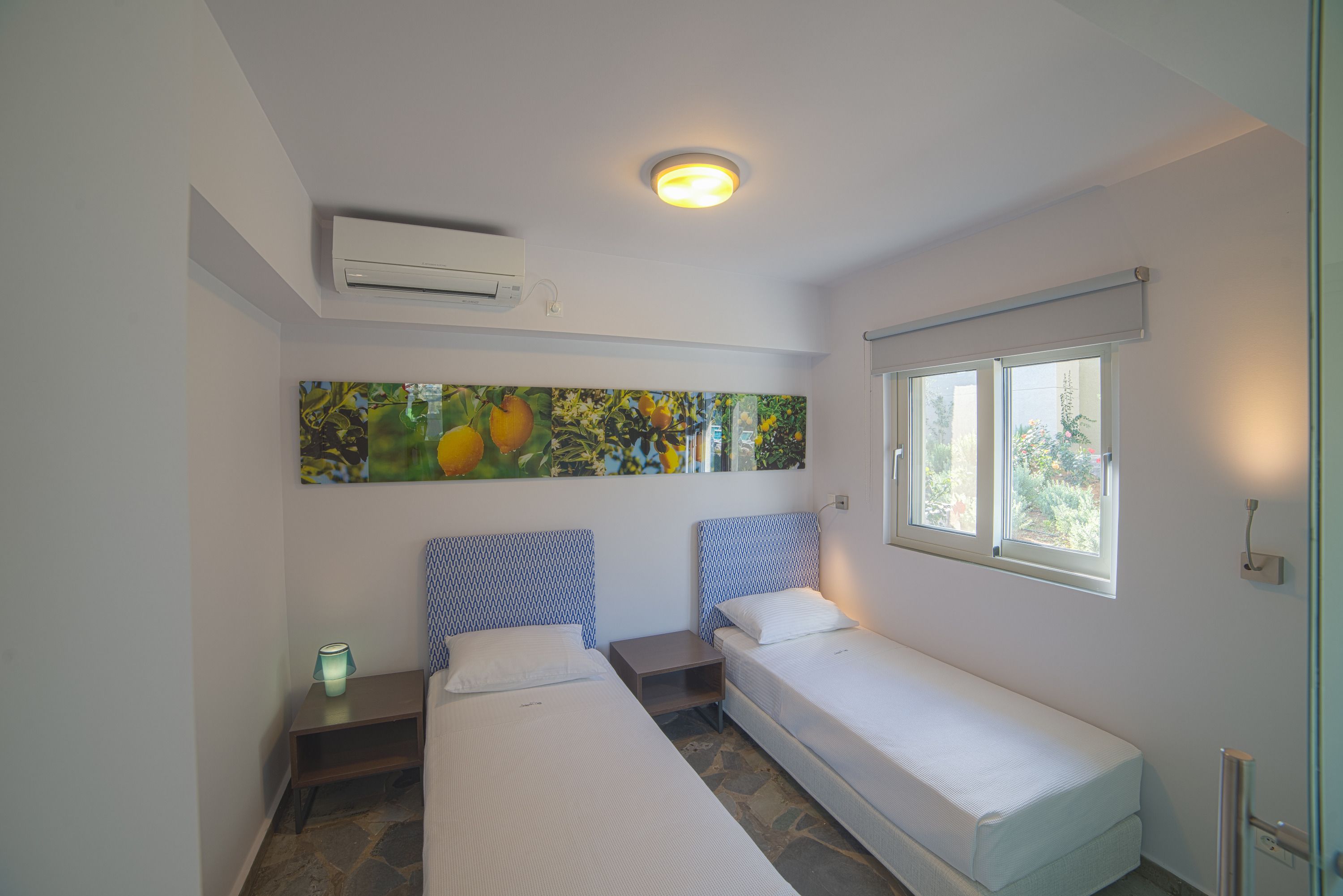 A bedroom with two beds, a ceiling light, an air conditioner, a window, and a painting on the wall.