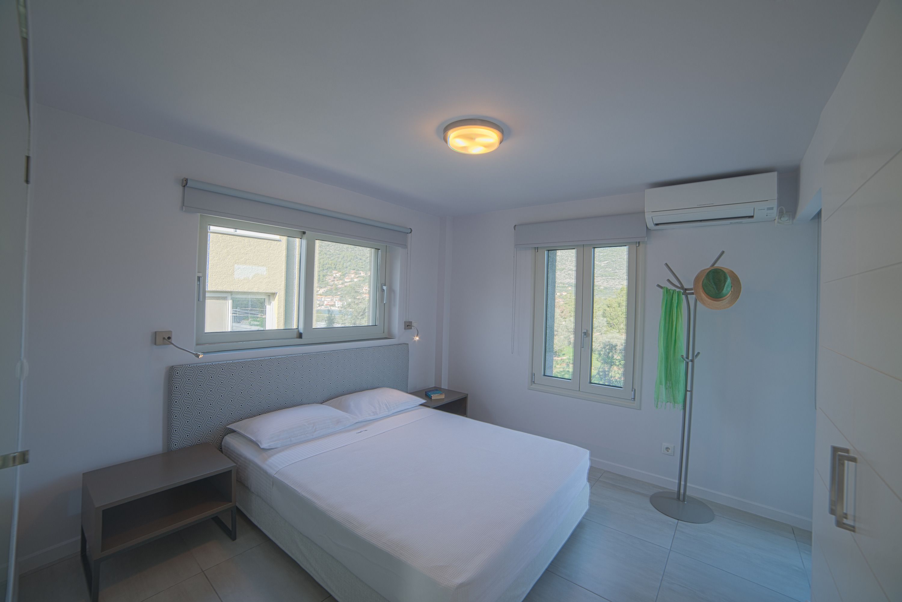 A bedroom with a bed, bedside tables, a standing lamp, and two windows.