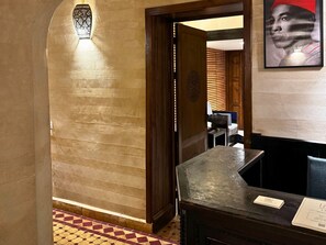 A hallway with a patterned floor, a wooden door, and a reception desk with a sign. - Riad Casa Lalla – Rooftop, Restaurant & Spa Medina (Marrakech)