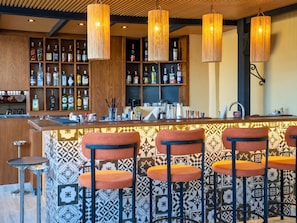 Un espace bar avec des étagères en bois remplies de bouteilles, un comptoir et trois tabourets de bar.