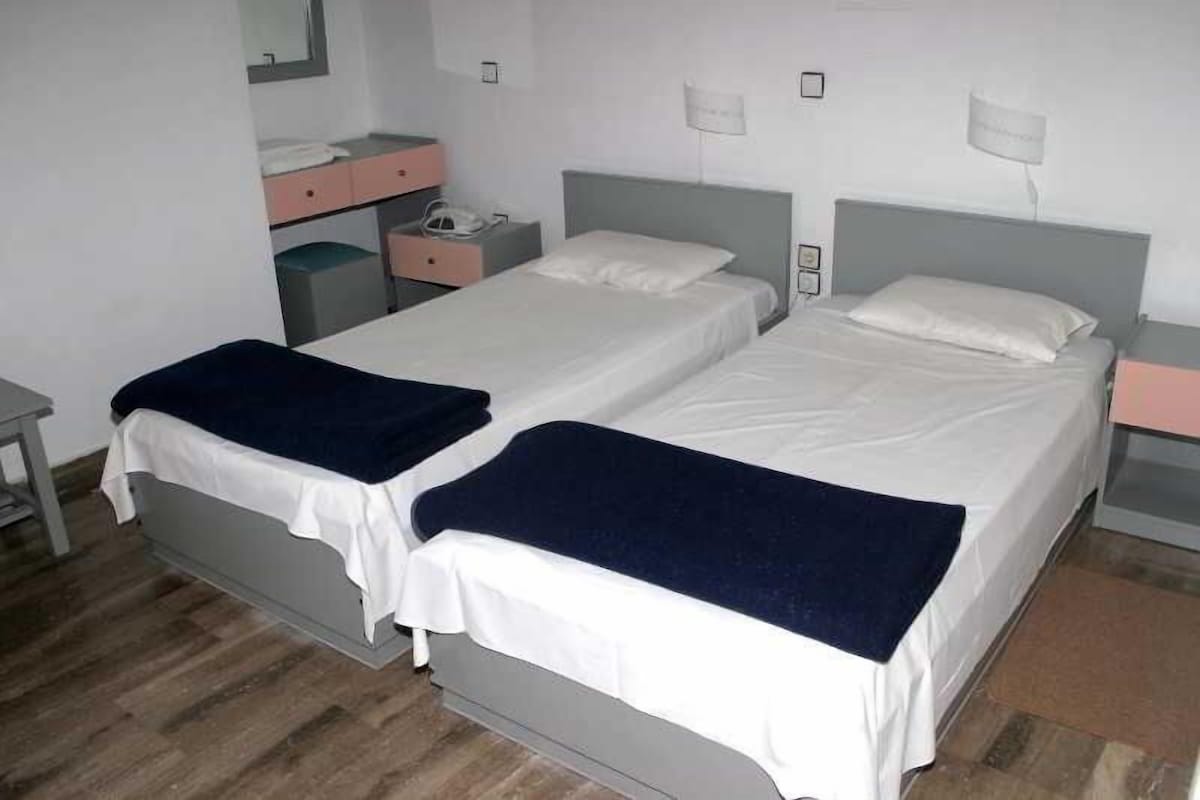 A double bed with a white and blue bedspread, a bedside table, a nightstand, a mirror, and a small dresser with a pink top.