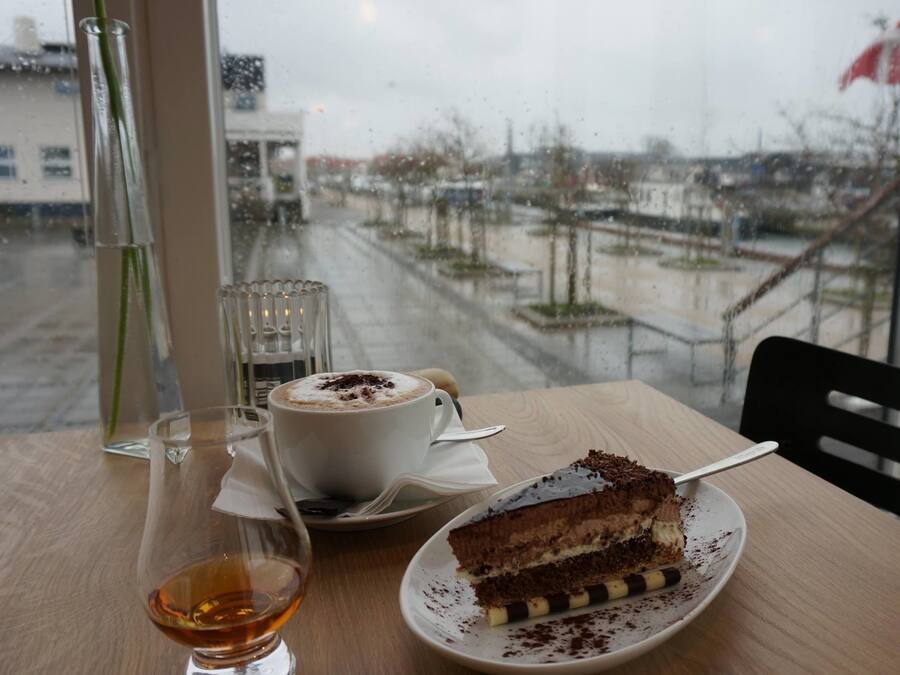 Ein Tisch mit Kuchenstück, einer Kaffeetasse und einem Whiskeyglas.