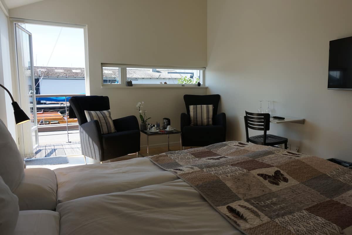 A hotel room with a bed, two chairs, a small table, a TV, and a window with a view of the outside.